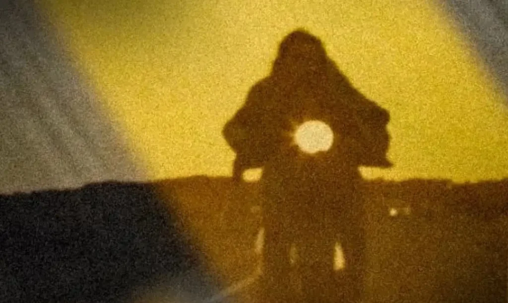 Silhouette of a person with a backpack standing on a hill against a yellow glow.