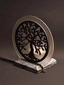 Oval metal pendant with a black tree silhouette inset, resting on a carved stone base against a dark background