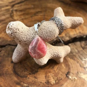 Pink teardrop gemstone pendant on a silver chain resting over a beige coral-like piece.
