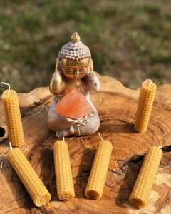 Bronze Buddha statue holding a pink crystal, set on a wooden stump with yellow beeswax candles around.