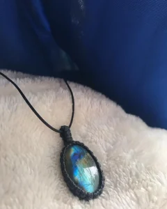 Oval labradorite pendant with blue-green iridescence in a black macrame bezel on a black cord.